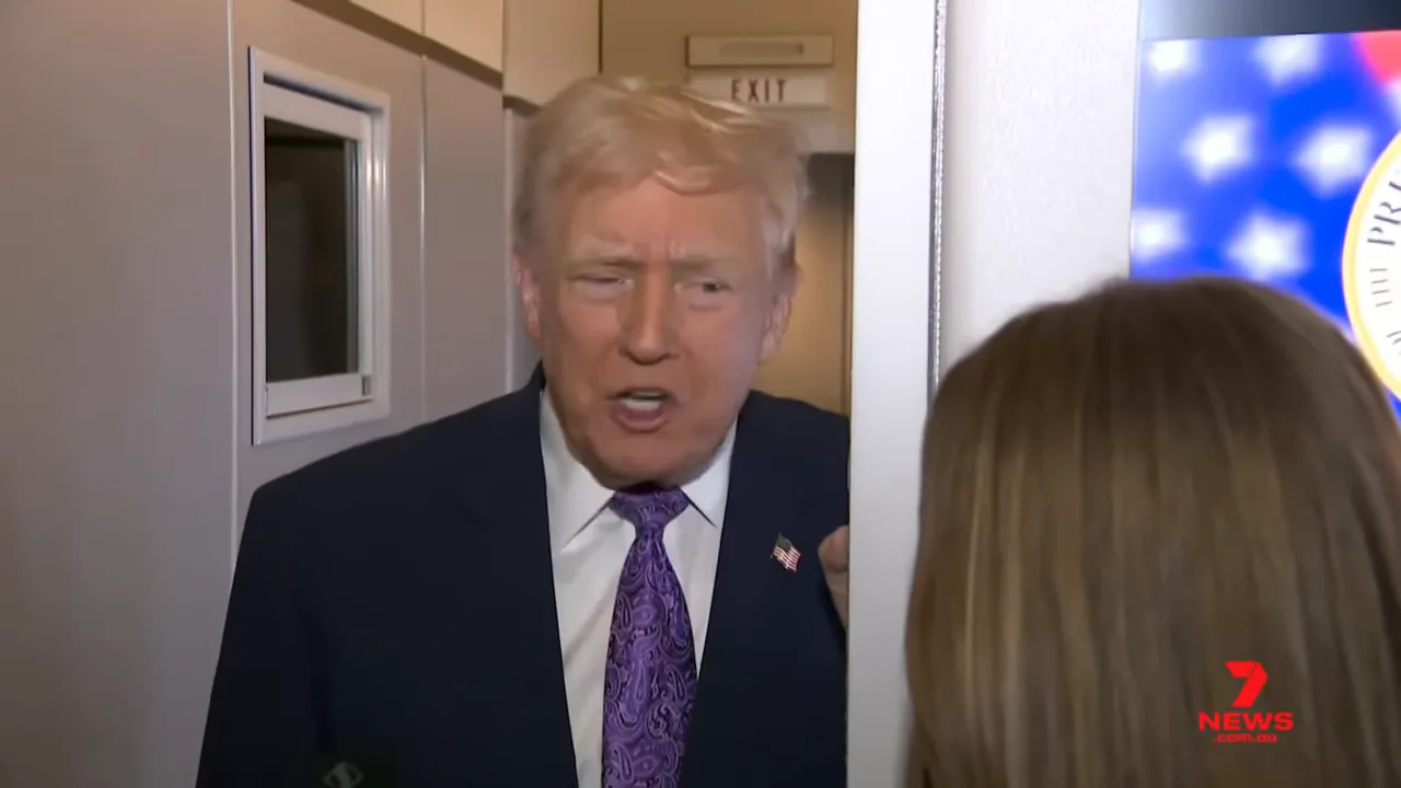 Senior official speaking emphatically from an aircraft doorway during a press exchange with reporters and a screen visible to the right