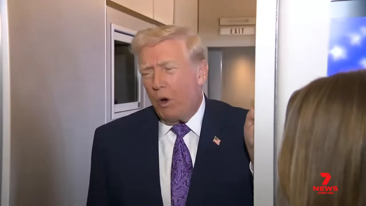 Man in a suit speaking to reporters from a doorway in a narrow cabin, caught mid-sentence.