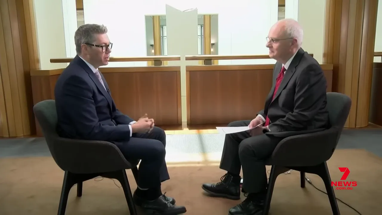 Two people seated facing each other in a formal interview setting showing whole chairs and surroundings