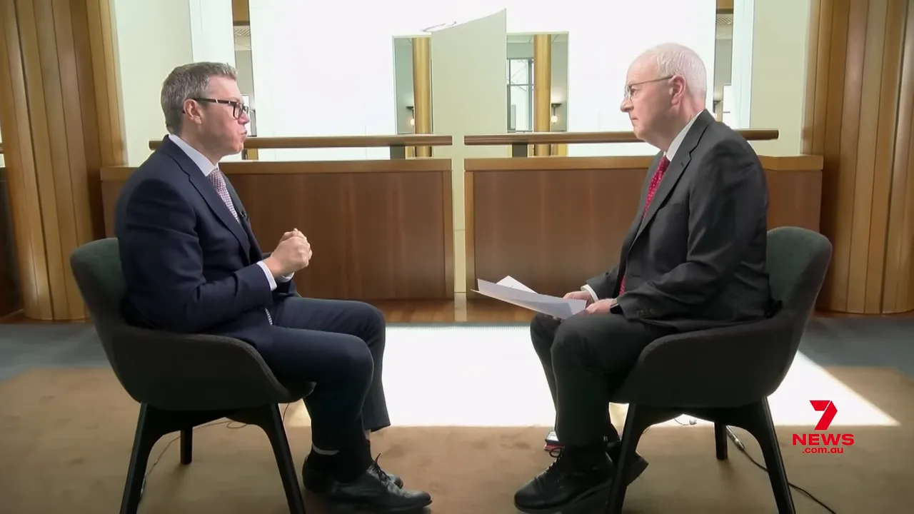 Two people seated facing each other in a well-lit interview setting, showing body language and discussion with papers visible between them.