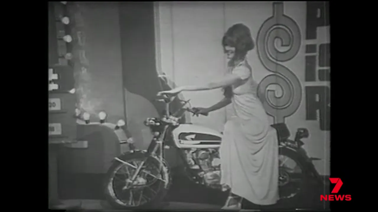 Vintage television show still: woman seated on a motorcycle on a stage set