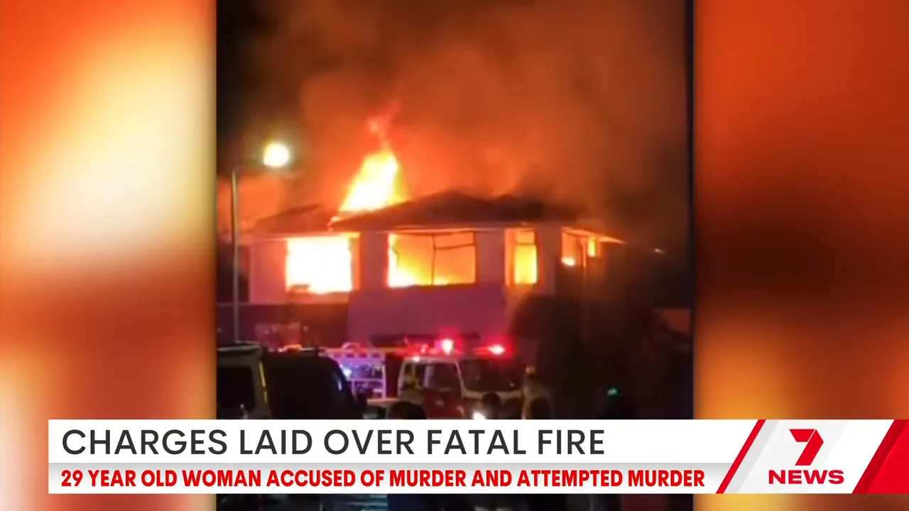 Two-storey house on fire at night with large flames visible through upper‑floor windows and emergency vehicle lights