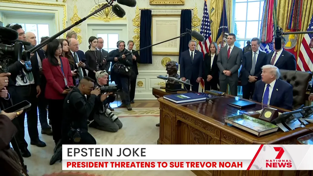 Wide shot of the Oval Office showing the President at the Resolute Desk with reporters, cameras and boom mics in foreground