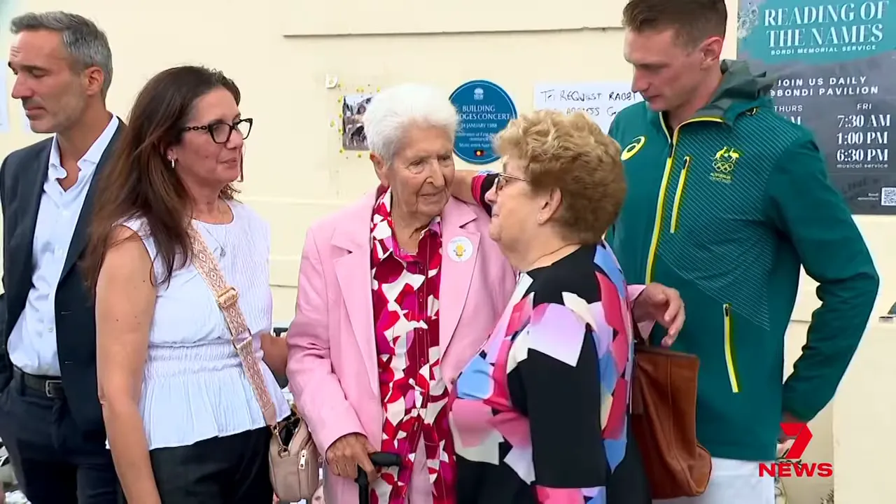 Group of sporting figures and community members speaking together at an outdoor memorial.