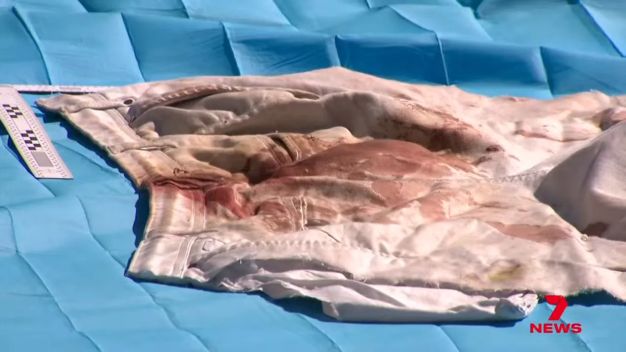 Bloodstained clothing laid out on a blue evidence sheet with a forensic measurement ruler visible