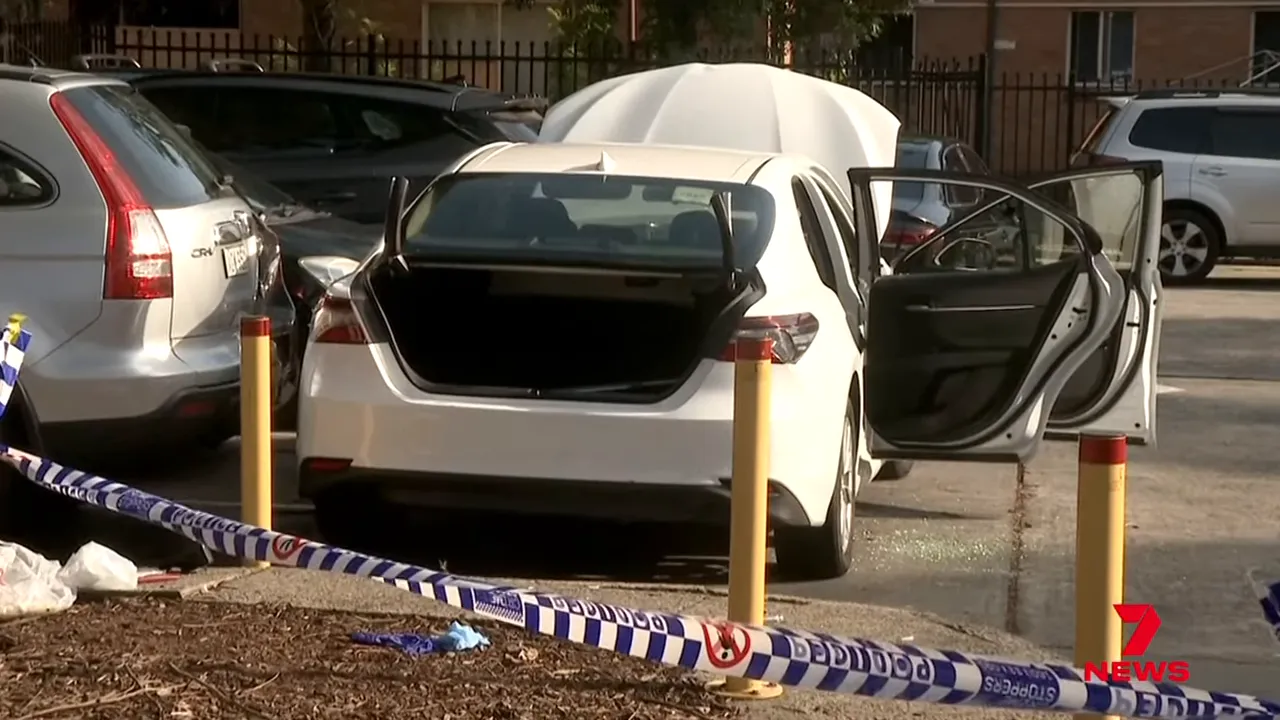 White Toyota Camry with its boot and rear doors open behind police tape in a cordoned parking area