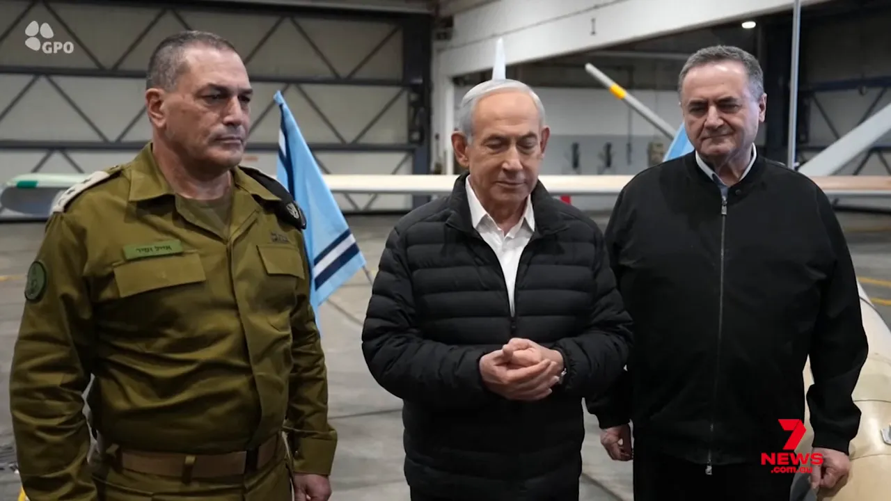 Three senior officials and a military officer standing in an aircraft hangar with aircraft and flags behind them.