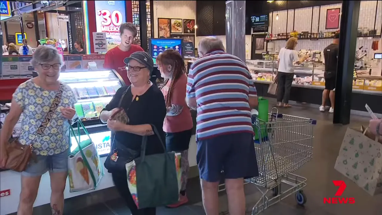 Group of shoppers smiling and chatting at a lottery kiosk inside the Colonnades shopping centre