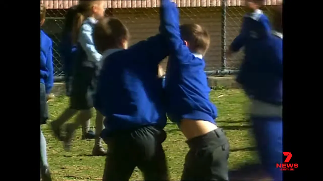 two primary-school children in blue uniforms grappling on a school field, illustrating imitative play