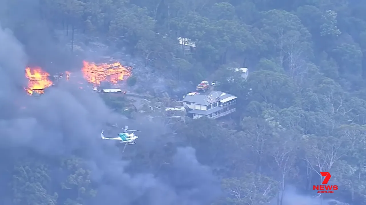 Helicopter and emergency vehicles near a house with flames burning very close in Koolewong