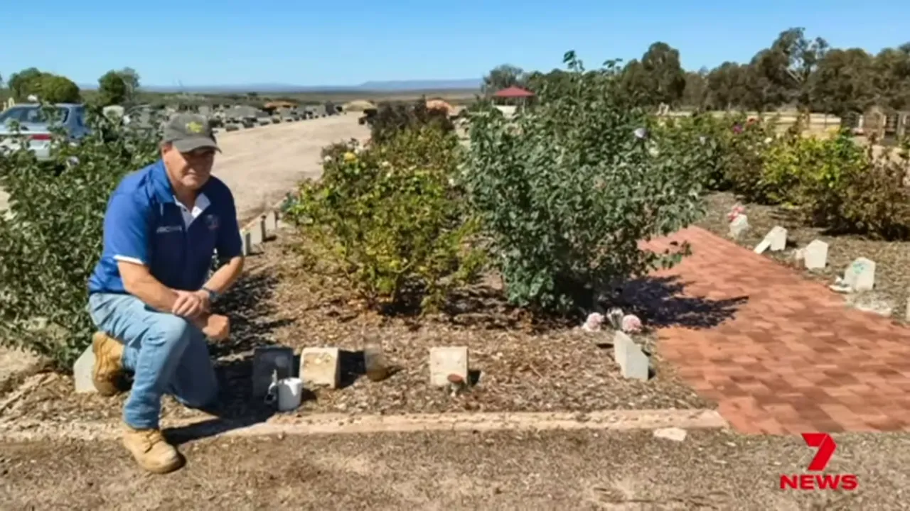 Person kneeling beside graves in Ashes Garden showing empty plaque mounts and missing brass plaques