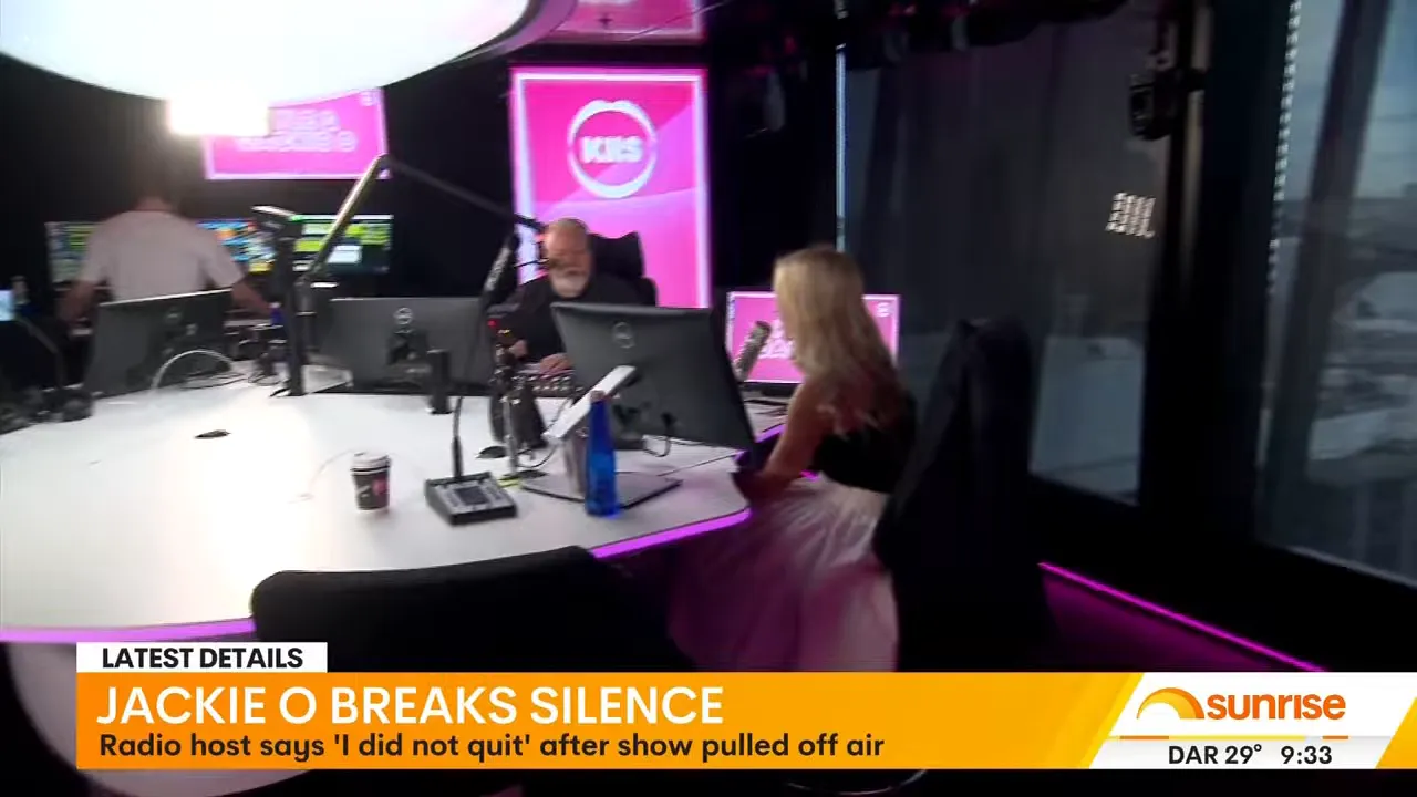 Wide shot of a radio breakfast show studio showing two hosts at the table, microphones, monitors and station branding.