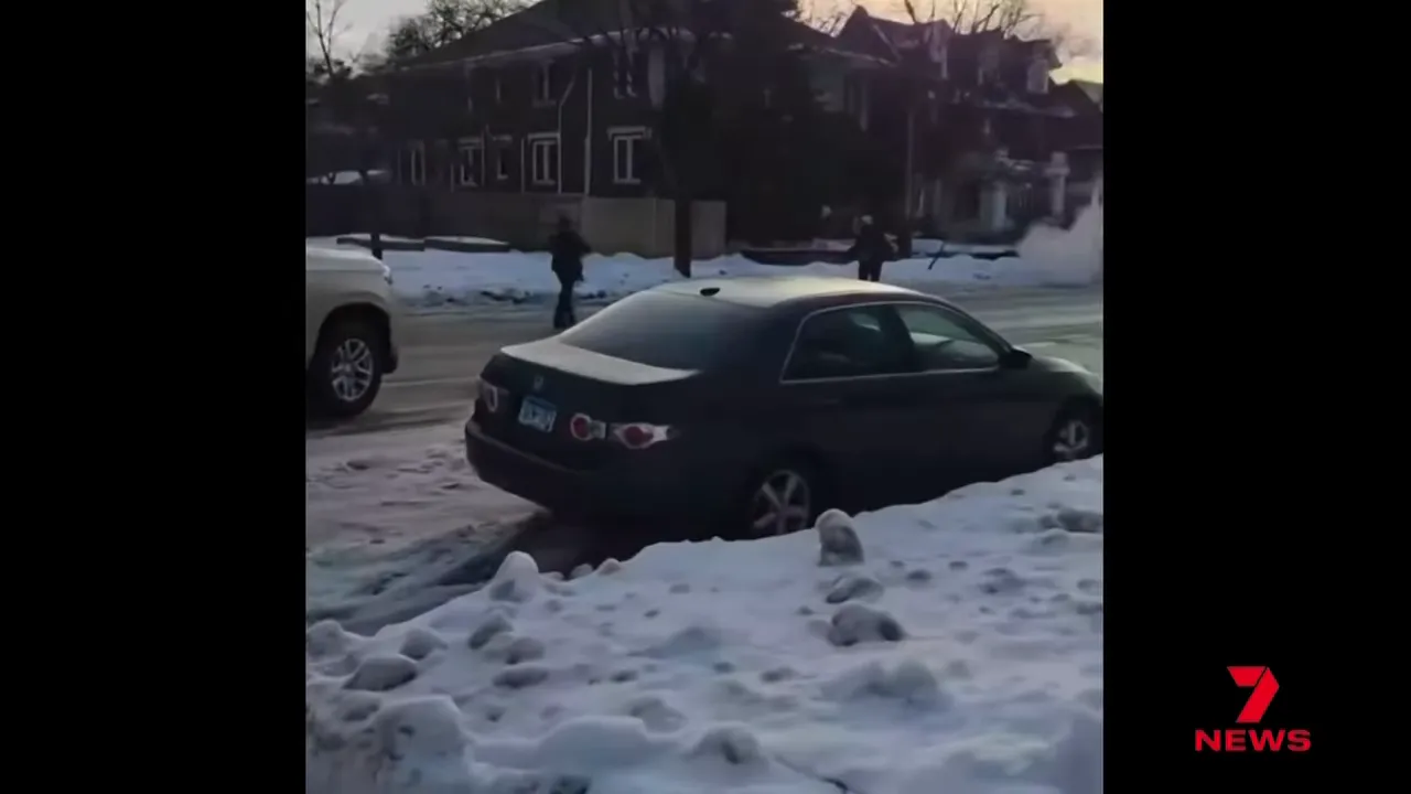 Dark sedan stuck in snow on a Minneapolis street with officers nearby during an ICE operation