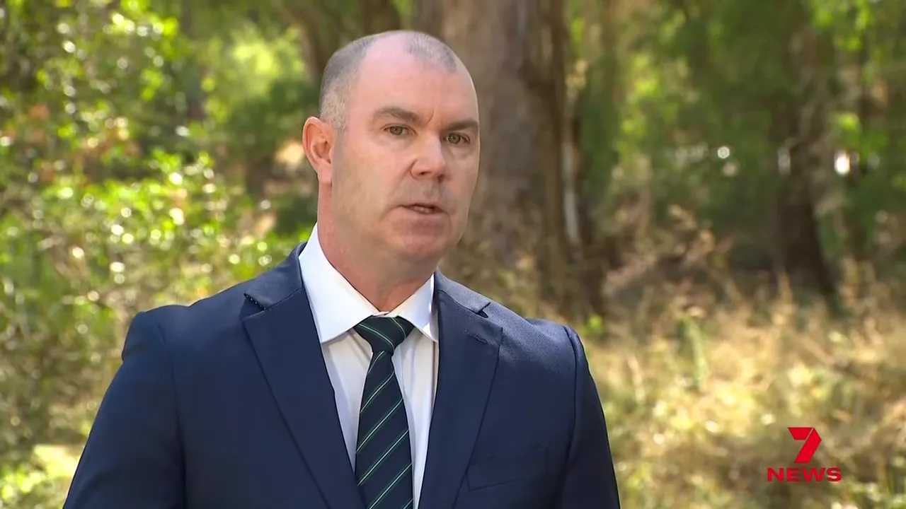Police spokesperson in suit speaking outdoors near bushland during the Mount Buffalo search briefing