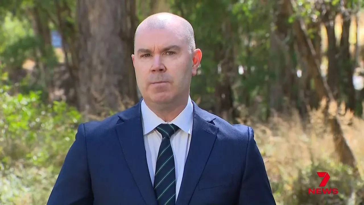Victoria Police spokesperson in suit speaking outdoors with bushland background