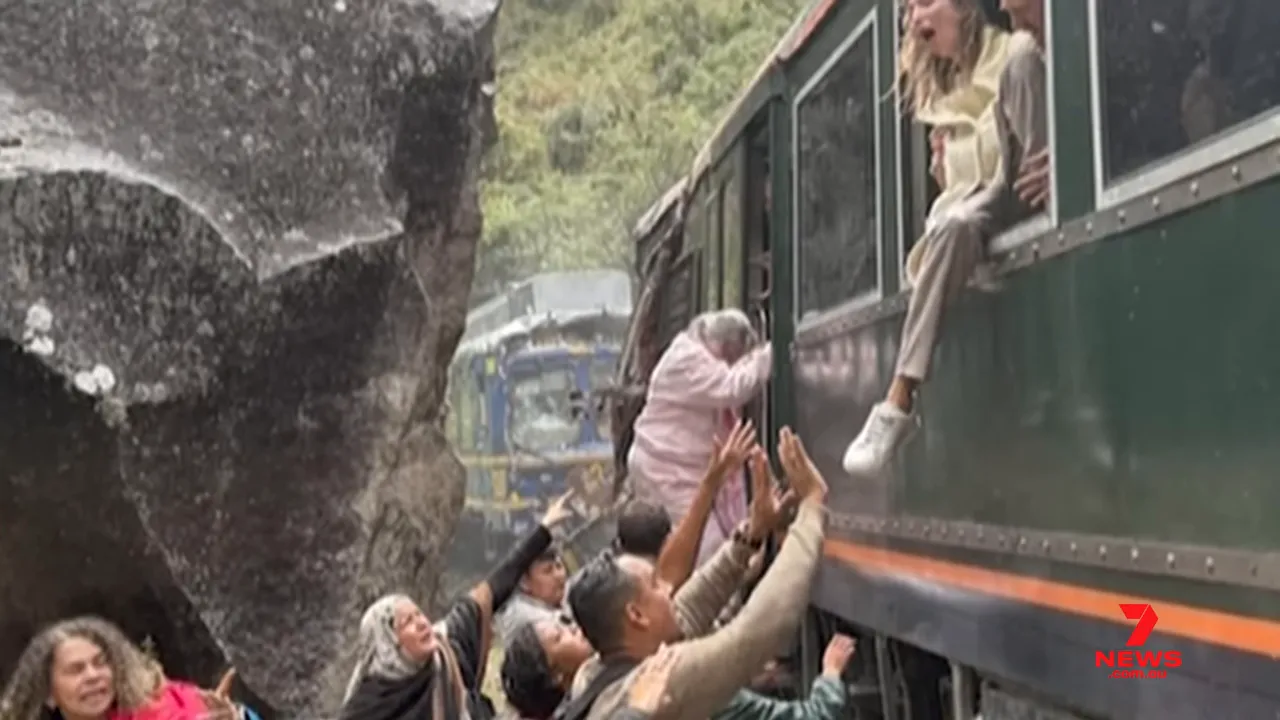 Passengers climbing out of a green train carriage with another train visible behind a rock