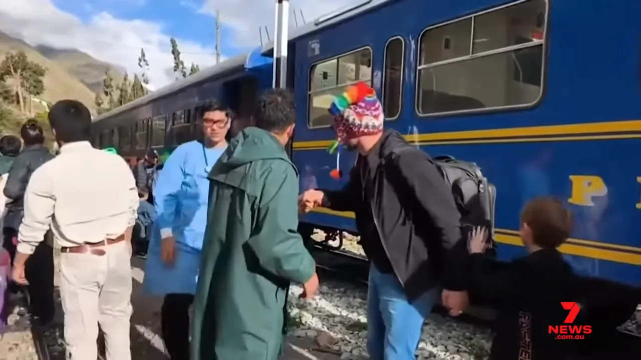 Passengers and rescue staff standing beside a blue train carriage on the tracks during evacuation