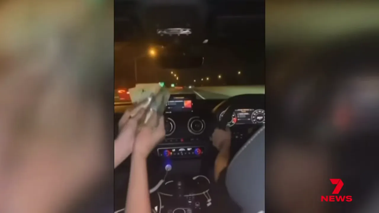 Interior night-time vertical phone video from inside a car showing a passenger waving cash with a driver at the wheel and a '7 News' logo