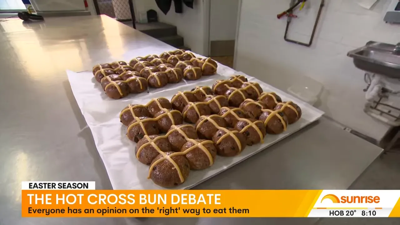 Tray of freshly baked hot cross buns with piped crosses cooling on a metal work surface in a bakery