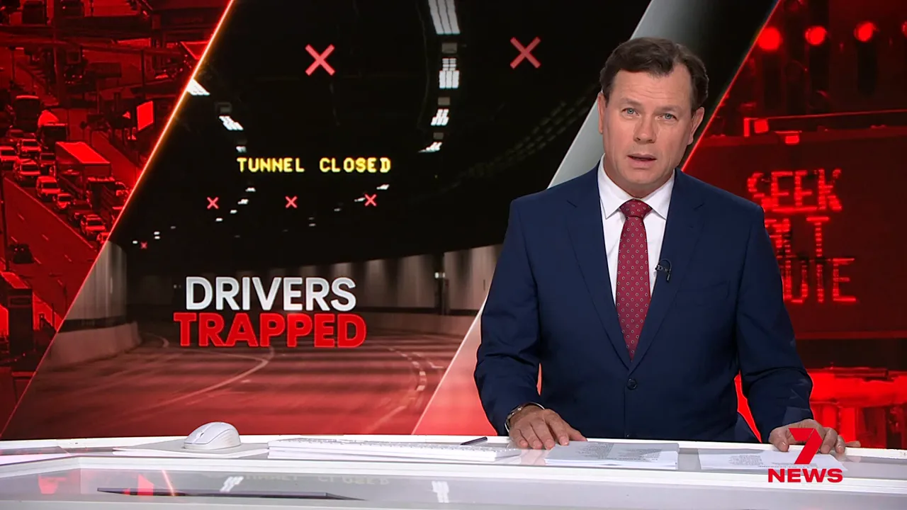Television news presenter beside a large graphic reading 'Drivers Trapped' and 'Tunnel Closed' with an image of an empty tunnel.