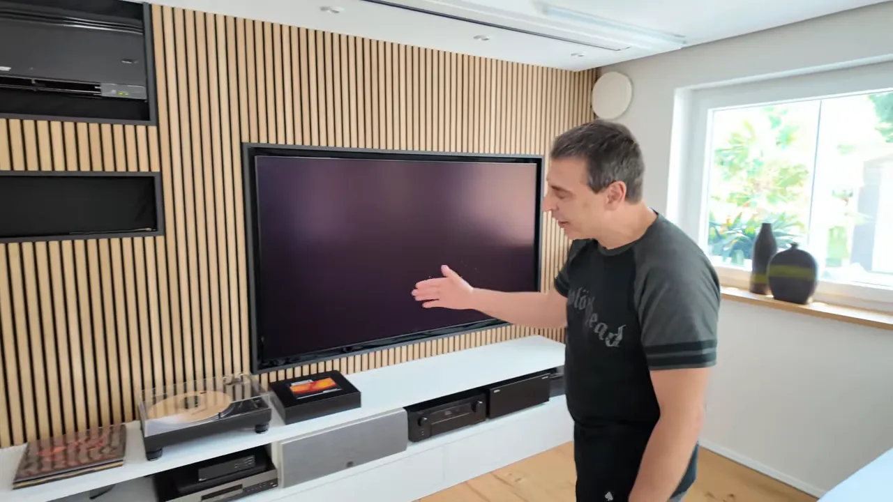 TV-Wand mit großem Fernseher, weißen Standlautsprechern, Medienmöbel und Holzlamellenverkleidung