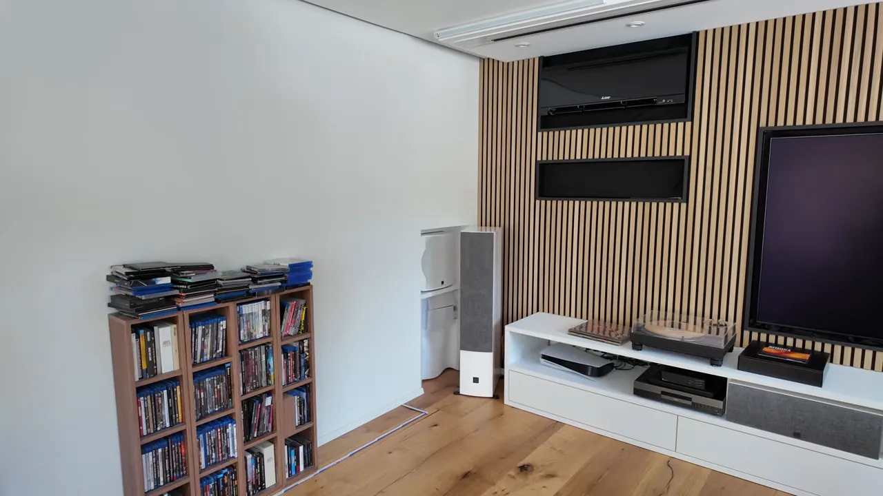 Weiße Wand neben einem Regal mit Blu-rays, Standlautsprecher und Holzlamellenwand