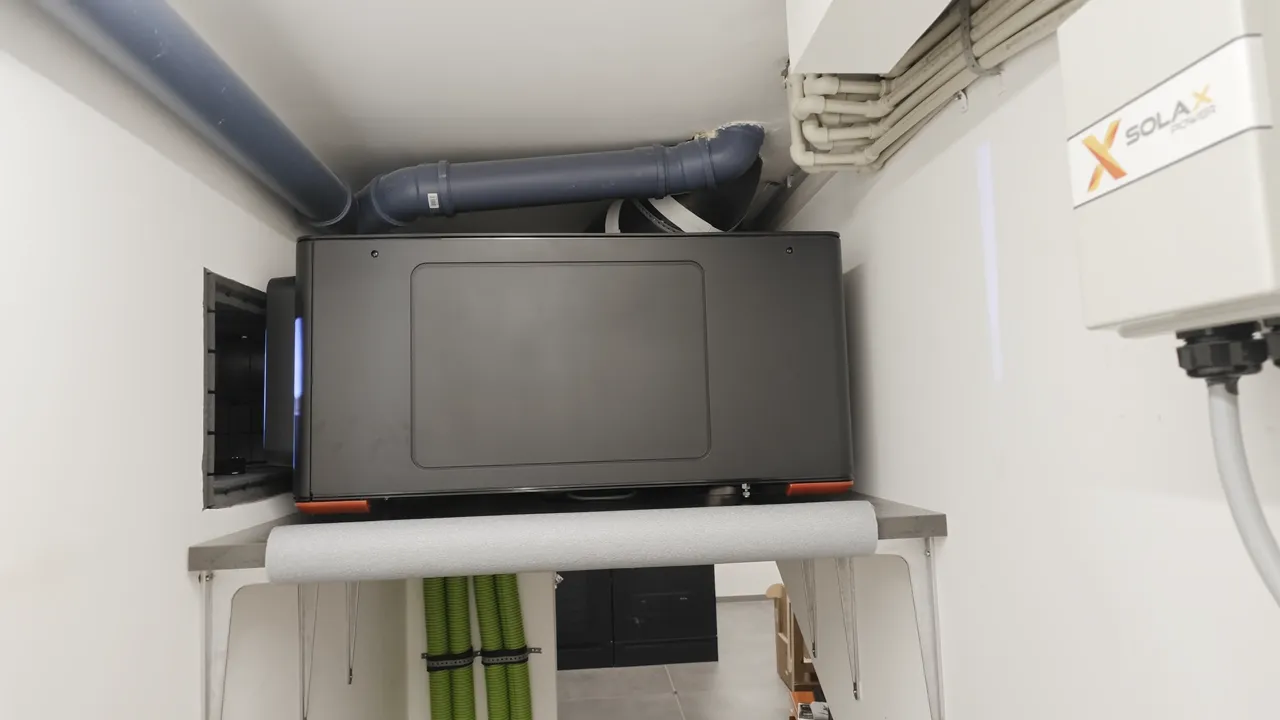 Großer grauer Projektor auf einer erhöhten Plattform im Technikraum mit Lüftungsrohr darüber