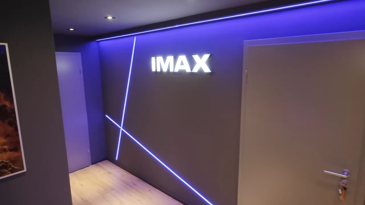 Kinovorraum mit beleuchtetem IMAX-Schriftzug, blauen Lichtlinien, Filmposter und geschlossener Tür