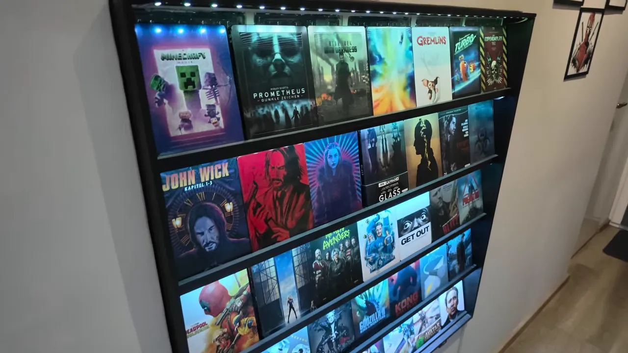 Beleuchtetes Wandregal mit ausgestellten Filmhüllen, darunter Prometheus, Gremlins, Turbo und John Wick
