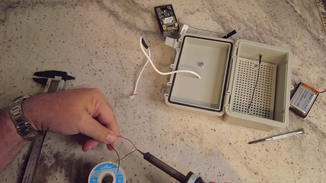 soldering iron joining red and black solar panel wires next to an open waterproof enclosure