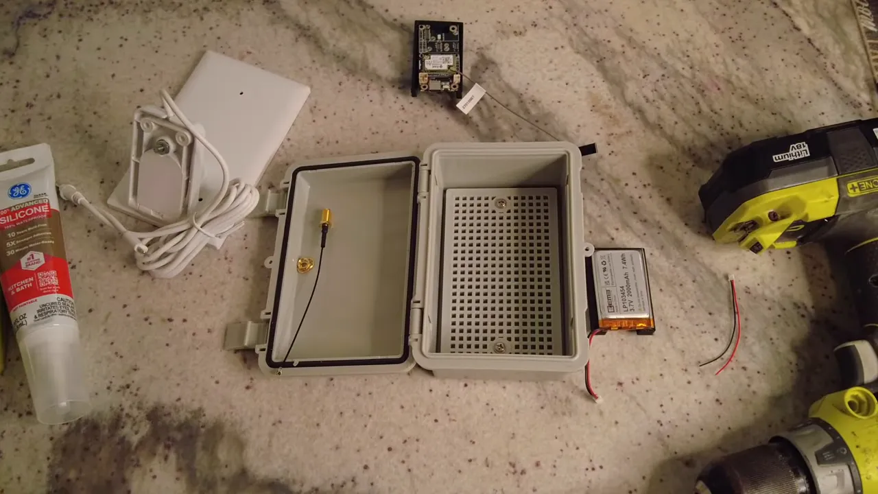 Open waterproof enclosure showing installed SMA pigtail, exposed battery, drill and cable ready for routing