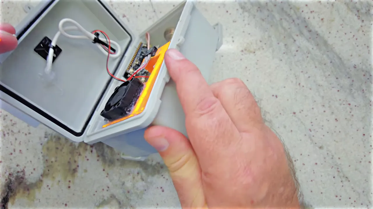 Internal enclosure showing a small fan mounted on orange ducting with wires and components visible