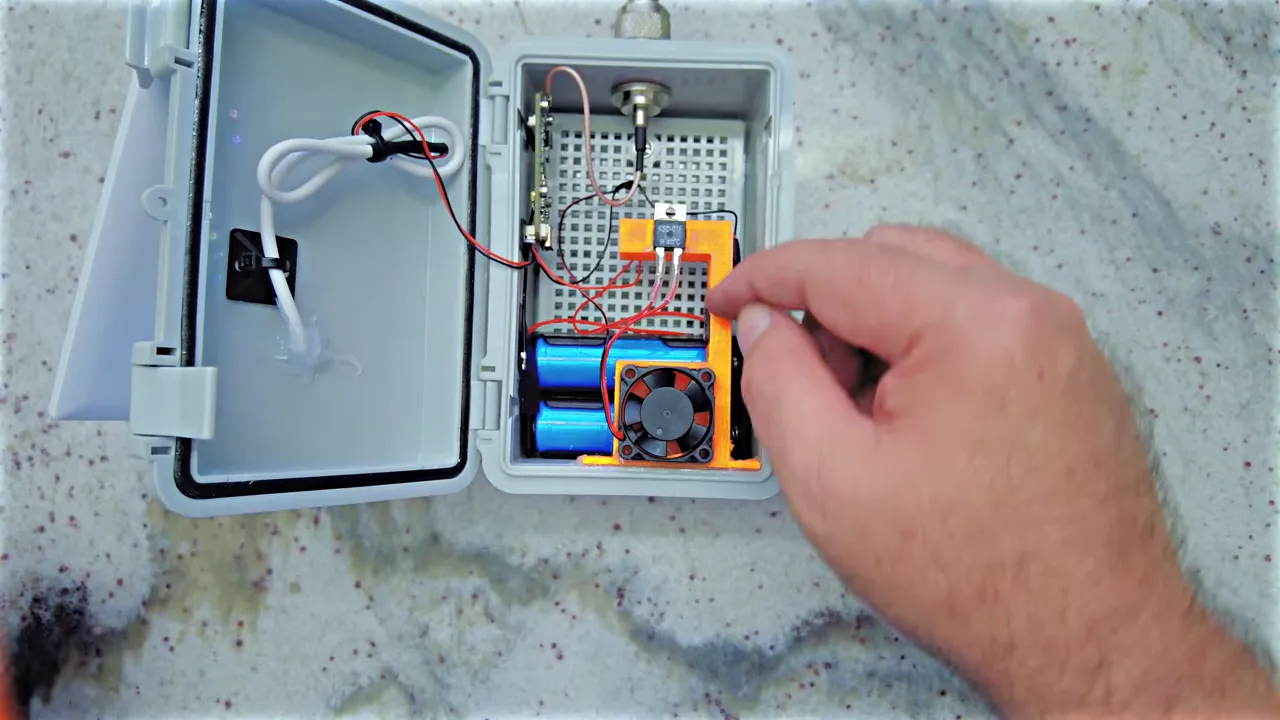 Top-down view of an electronics enclosure with an orange 3D‑printed duct, small fan, 18650 batteries and wiring