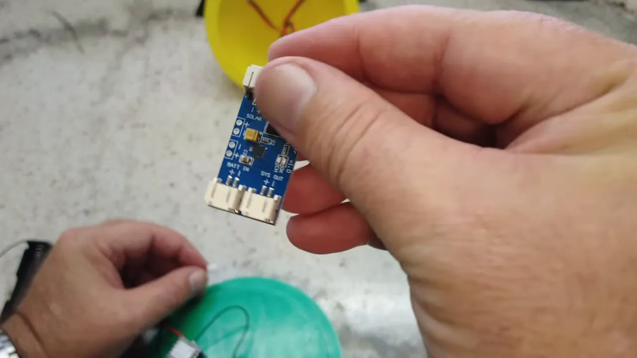 Close-up of a blue solar charge controller board held between fingers showing JST ports and PCB markings