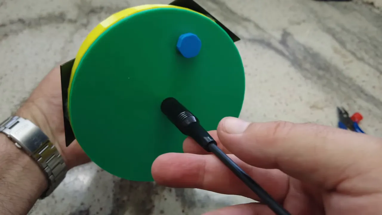 Close-up of the Meshtastic tree node green base with antenna connector inserted and hands holding the device