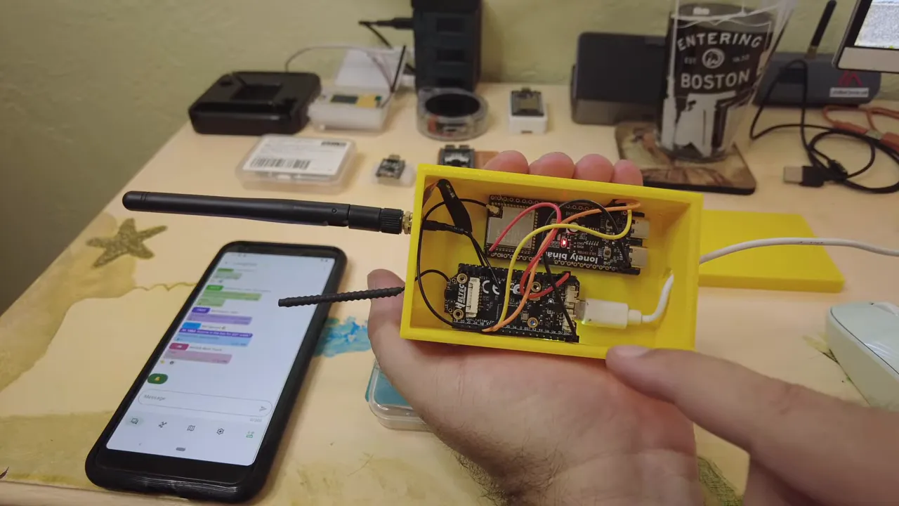 ESP32-S3 enclosure with internal wiring held in-hand next to a phone displaying a messaging interface
