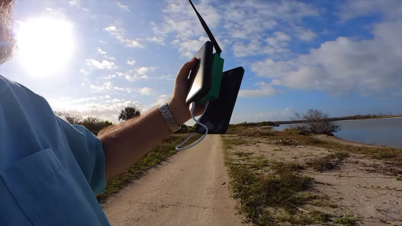 Hand positioning LoRa receiver antenna outdoors on a beach path near the water
