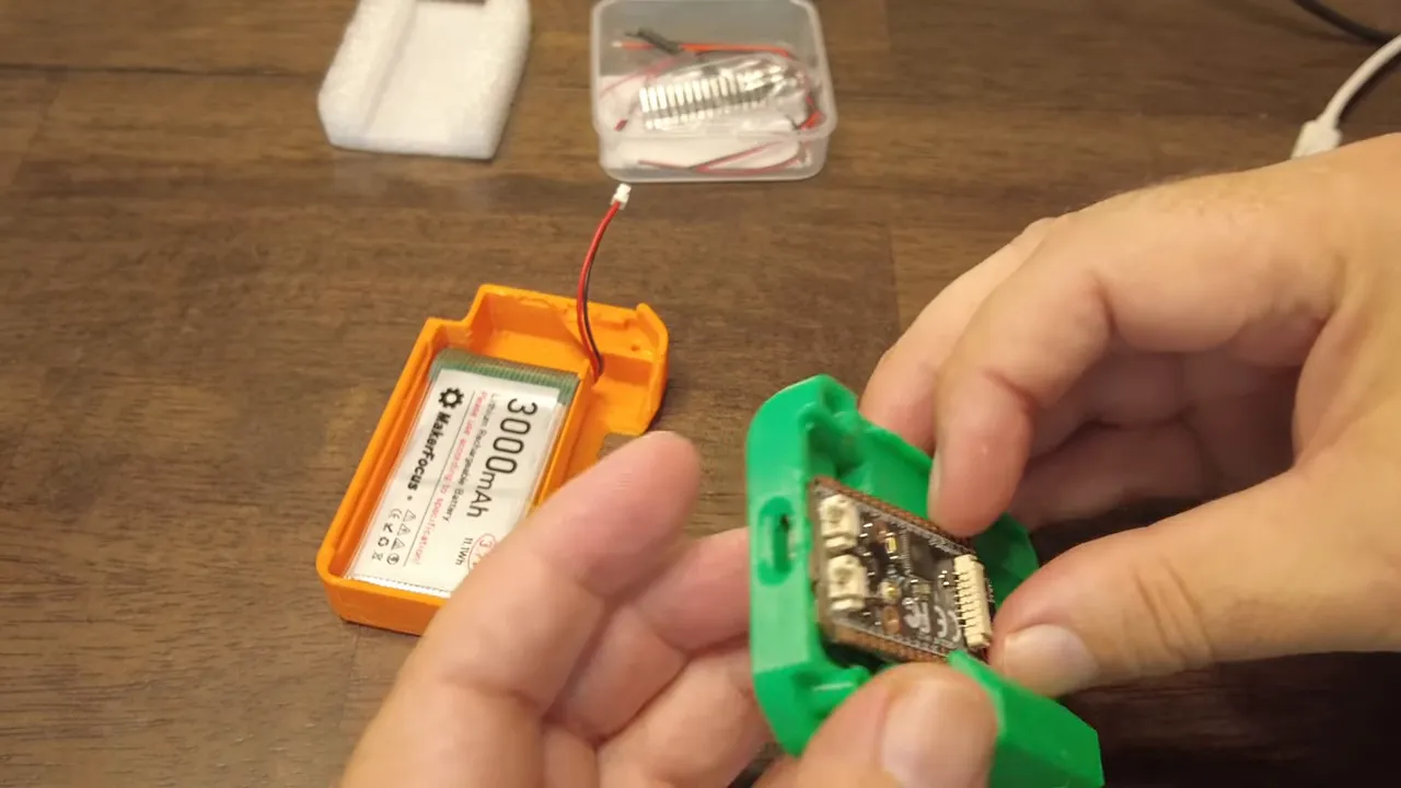 Green 3D-printed Heltec case being fitted with the board while an orange case with a 3000mAh battery and red-black connector sits open in the background