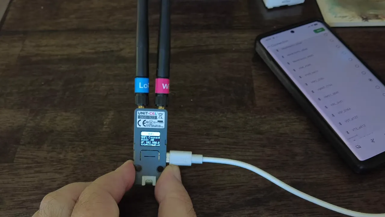 M5Stack C6L module plugged in by USB showing 'WiFi Connect' and its local IP address on the device display, with a phone nearby.