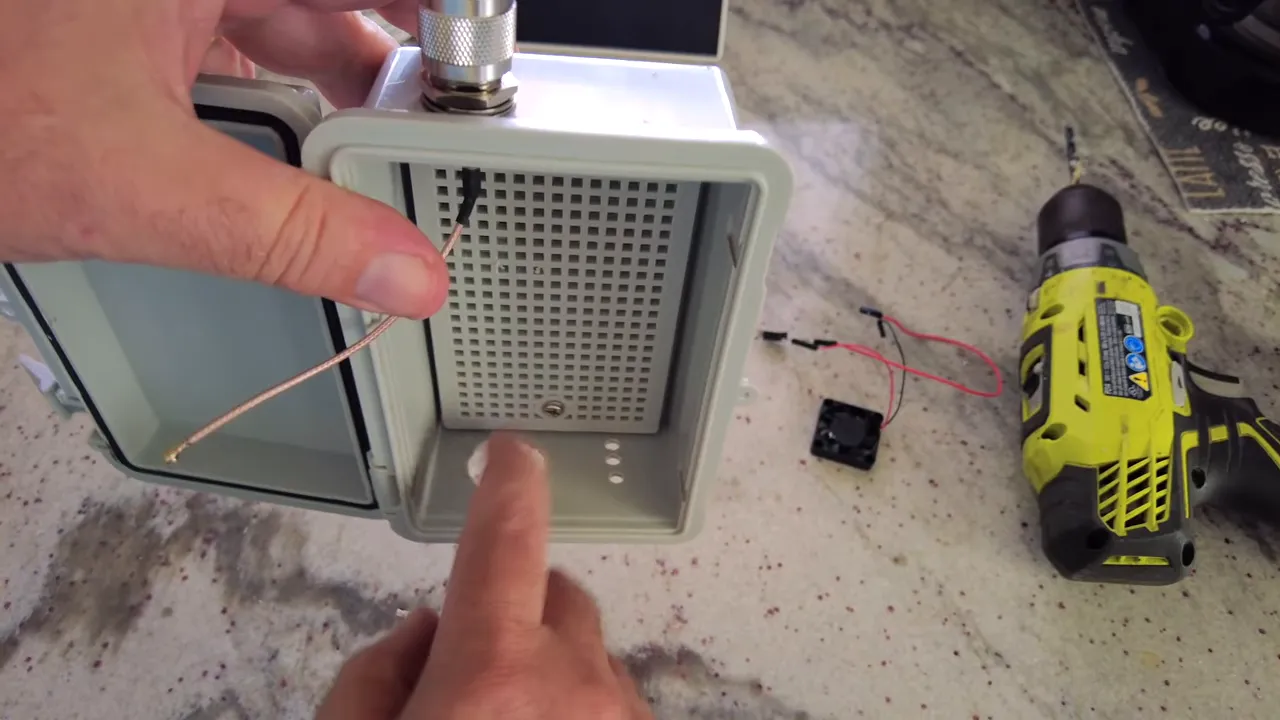 Open waterproof enclosure interior showing drilled intake holes, antenna coax, and nearby fan wiring