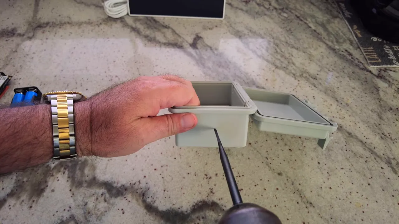 Drill bit pointed at the side of a plastic enclosure indicating the antenna hole location