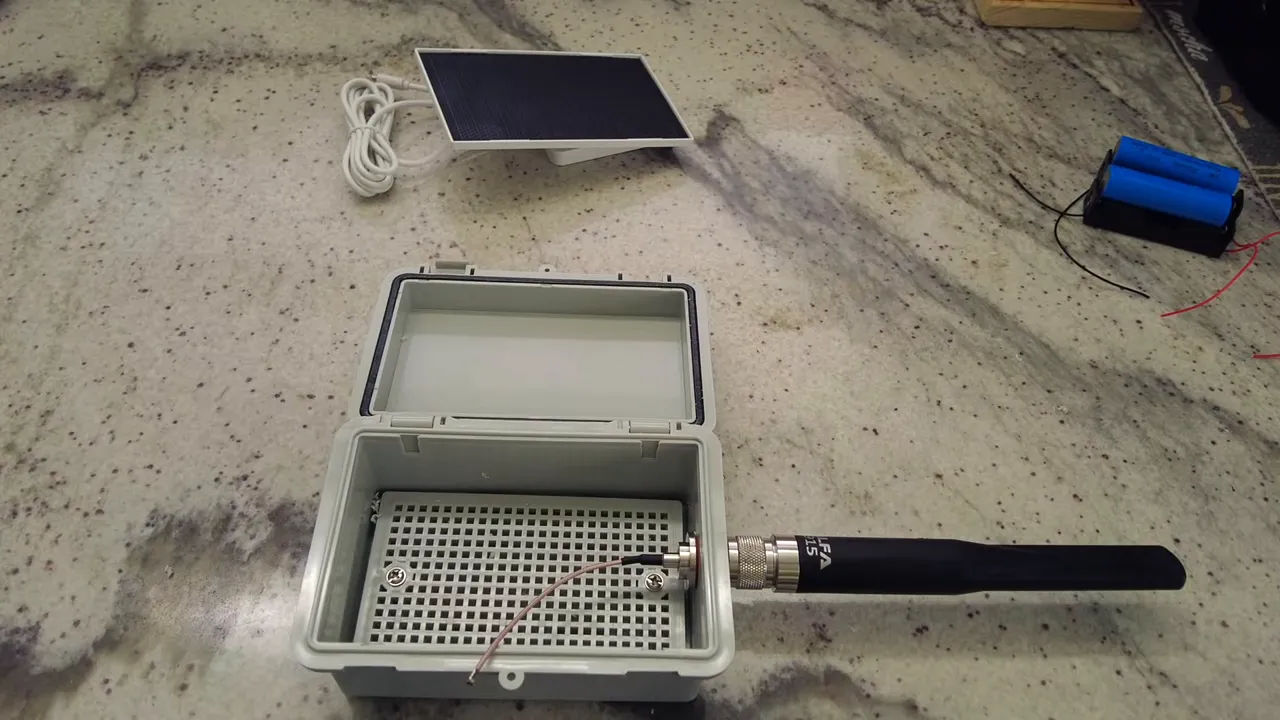 Open waterproof electronics enclosure with Type N antenna attached, small solar panel and two 18650 cells in a holder on the counter.