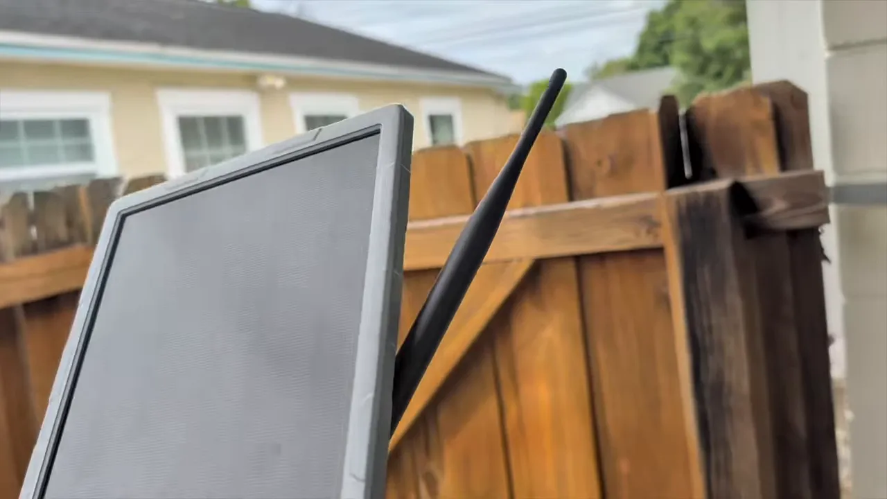 Side view of the solar repeater showing the panel angle and antenna in front of a wooden fence
