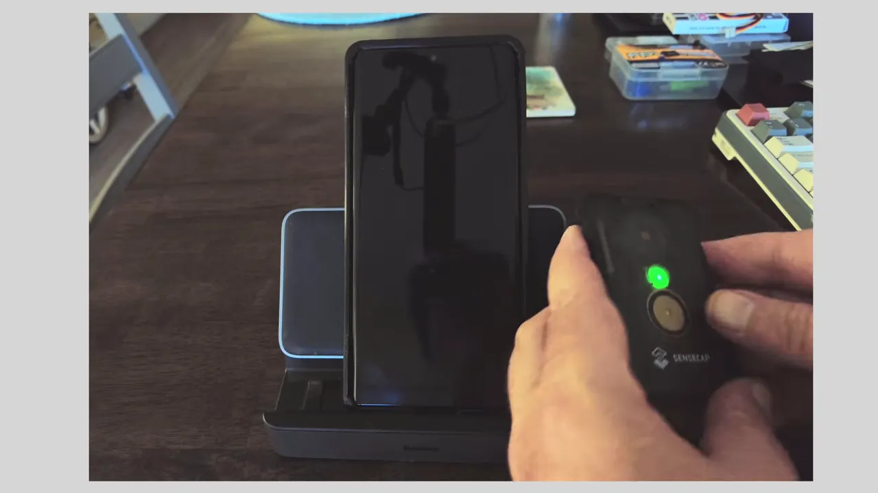 Seeed T-1000E being positioned beside a phone on a charging dock with green power LED