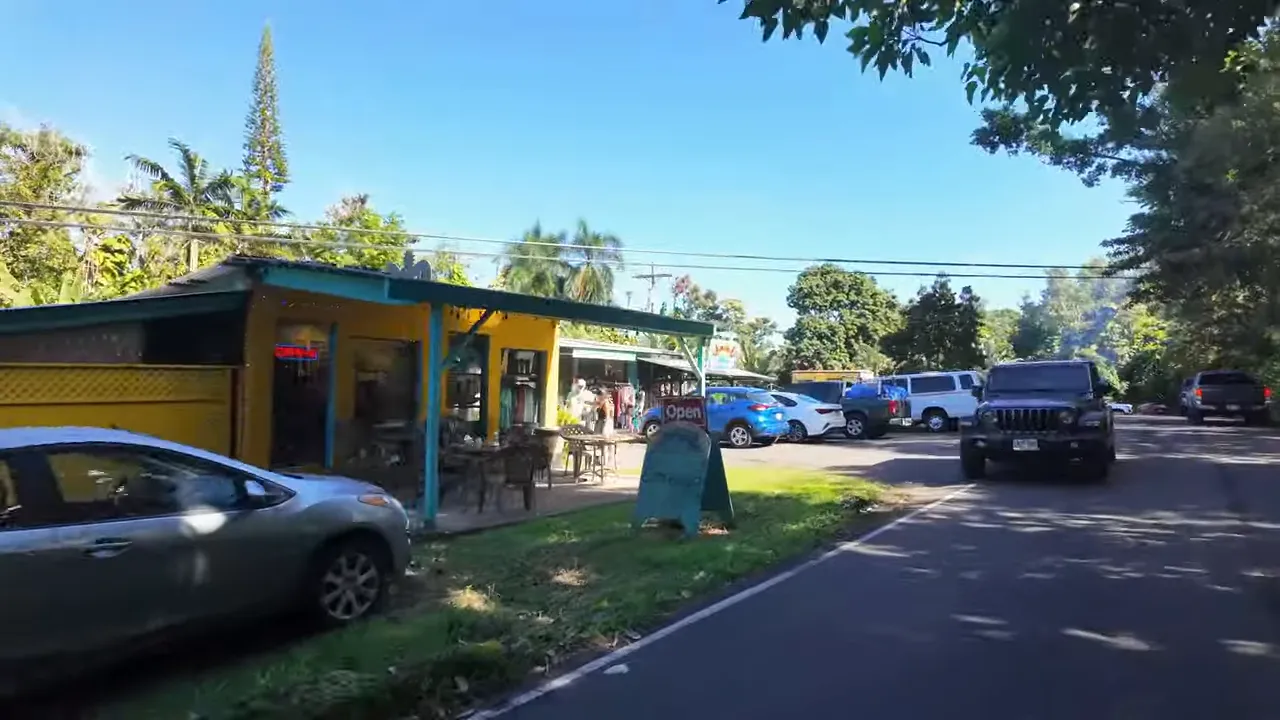 Colorful roadside shopfronts and parked cars along the road at Nahiku Marketplace