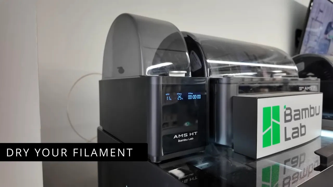 Close-up of a Bambu Lab AMS HT filament dryer enclosure with spool storage and overlay text 'DRY YOUR FILAMENT'