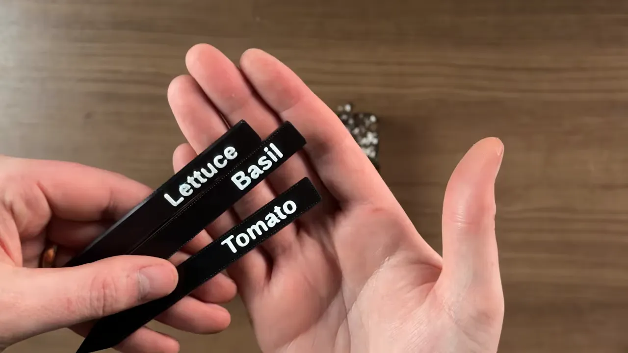 three black plant labels with white text reading Lettuce Basil and Tomato