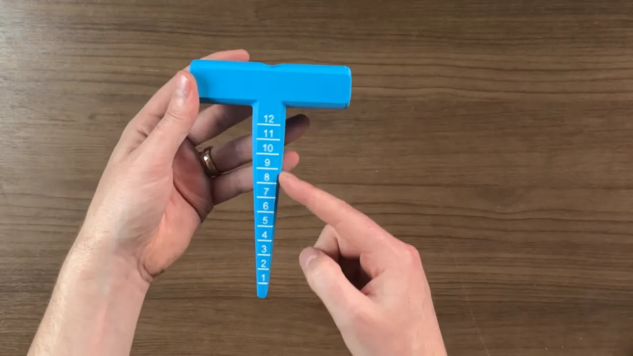 blue seed planter tool with depth markings held over a wooden table