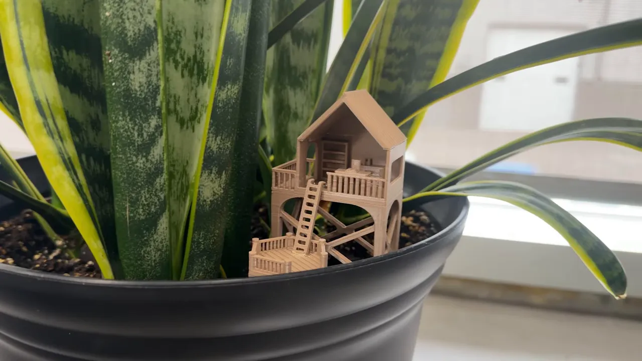 small treehouse decoration placed inside a black plant pot beside green leaves
