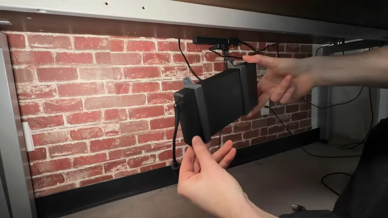 Hands installing a 3D printed charger bracket under a desk to hold a power brick